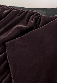 Plüsch-Veloursstoff in tiefem Burgunderrot, mit sanften Drapierungen und einer glatten Textur, und einem schwarzen elastischen Taillenbund oben.