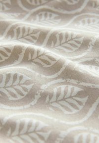 Tissu beige clair présentant un motif de feuilles répété en blanc doux, affichant une texture lisse et des détails de conception subtils.
