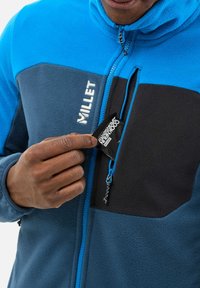 Blue and gray fleece jacket features a half-zip, zippered chest pocket, and the brand "Millet" in white on the front. Textured fabric.