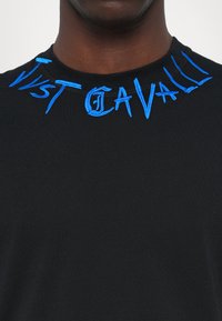 Svart bomulls t-shirt med broderad blå text på halsringningen som säger "Just Cavalli." Slät tyg med en klassisk rund halsdesign.
