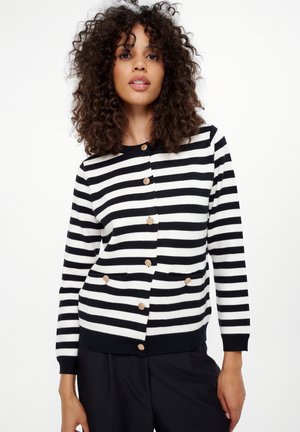 Striped cardigan in black and white, featuring round neckline, front buttons, and two pockets with wood-like accents. Soft knit material.