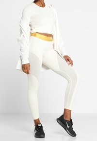 Conjunto atlético blanco que incluye una camiseta ajustada de manga larga y leggins de tiro alto con paneles texturizados. Destacado con una cinturilla dorada.