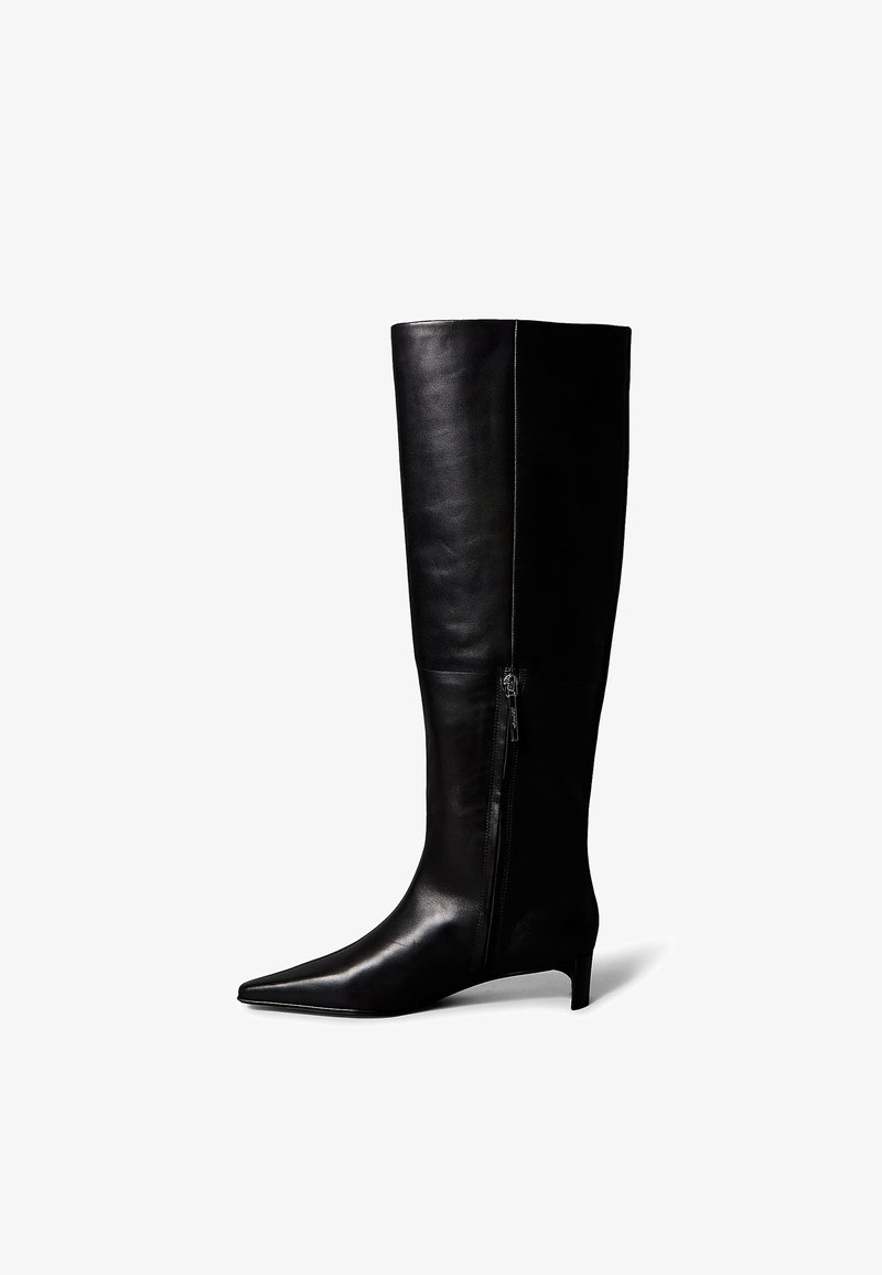 Botas negras de cuero hasta la rodilla con punta afilada y tacón bajo y delgado. Cuentan con cremallera lateral para facilitar el calzado y una textura suave.