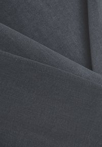 Tejido gris oscuro con una textura fina plegado sobre sí mismo, creando suaves capas superpuestas y sombras sutiles.