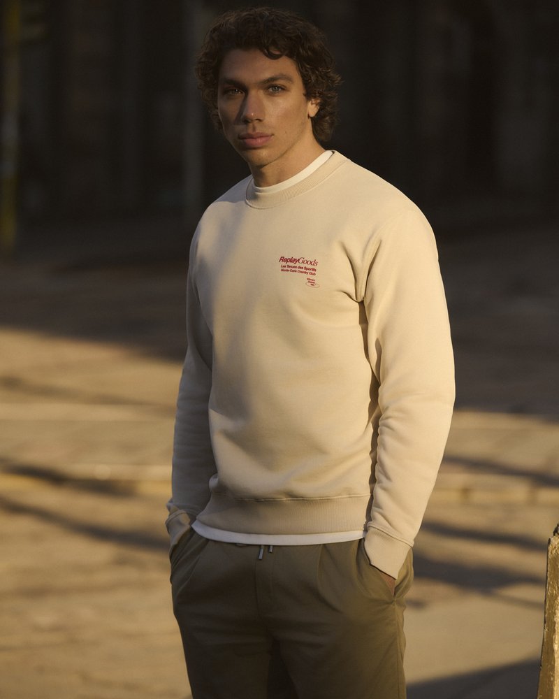 Beige crewneck sweatshirt with embroidered red logo on chest, paired with olive green pants, featuring a close-fitting design and smooth texture.