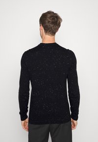 Schwarzer Pullover mit langen Ärmeln und einem strukturierten, gesprenkelten Muster, aus weichem Strickmaterial; taillierte Passform mit Rundhalsausschnitt.