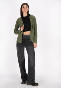 Oliwkowy hoodie na zamek, noszony na czarnym, skróconym topie, w połączeniu z czarnymi, wysokim stanem, szerokimi dżinsami oraz czarnymi, masywnymi butami.