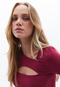 Burgundy paita, jossa on leikattu yksityiskohta, pehmeä kangas ja pyöreä pääntie. Sileä tekstuuri ja lyhyet hihat.