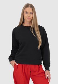 Felpa nera con collo a giro e maniche raglan, abbinata a pantaloni rossi larghi, caratterizzati da una superficie liscia e un design informale.