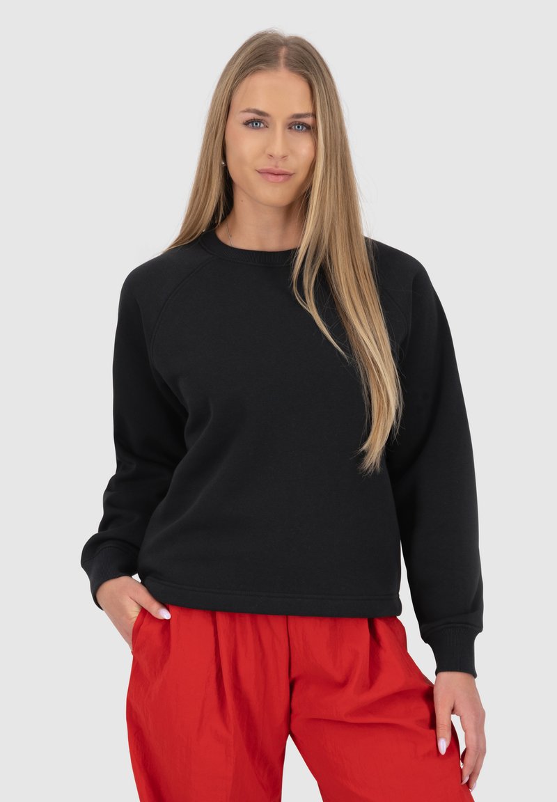 Felpa nera con collo a giro e maniche raglan, abbinata a pantaloni rossi larghi, caratterizzati da una superficie liscia e un design informale.