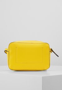 Borsa gialla in pelle con forma rettangolare, superficie texturizzata, chiusura con zip e piccola tracolla. Presenta cuciture e un dettaglio a patch sul retro.