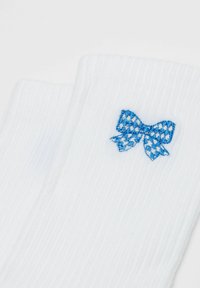 Weiße gerippte Socken mit einer kleinen blau-weiß karierten Schleife, die nahe dem Bündchen gestickt ist.