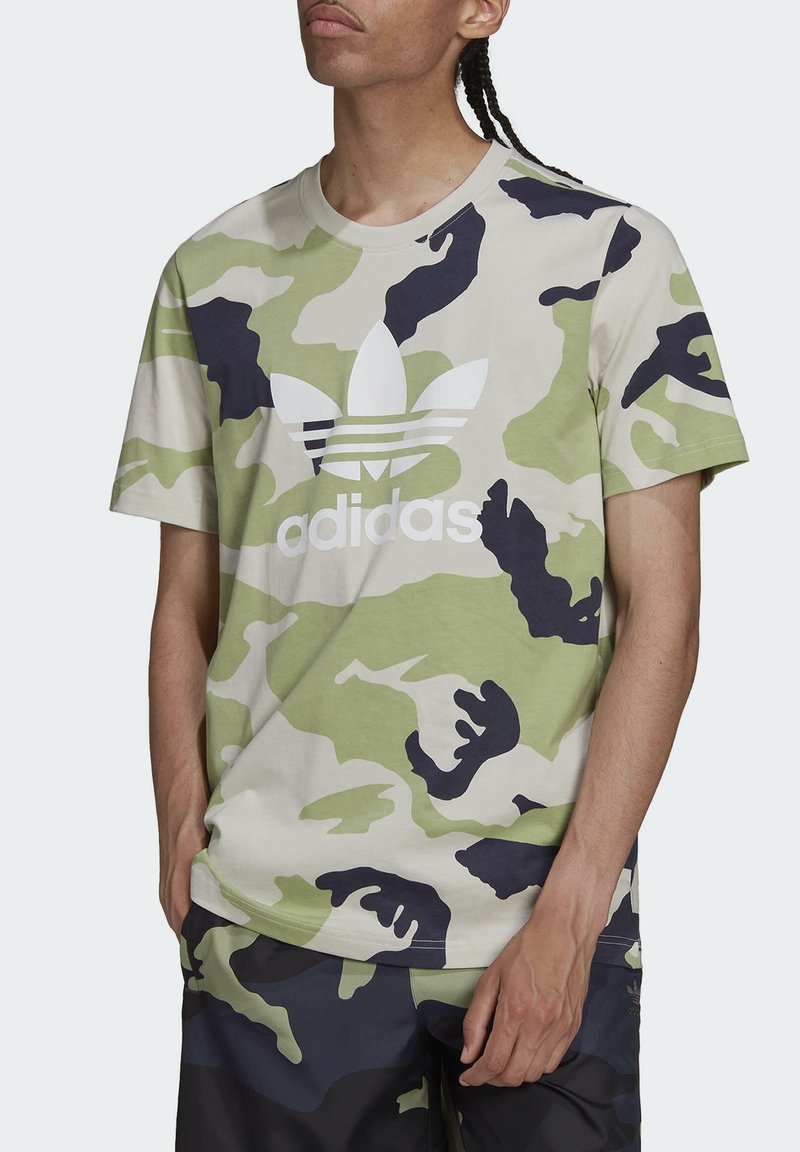 T-shirt camouflage in verde, beige e blu navy, con un grande logo Adidas bianco. Maniche corte e silhouette a girocollo.