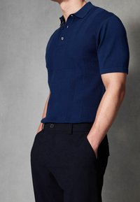 Polo bleu marine à texture côtelée avec des rayures verticales, patte de boutonnage trois boutons et manches courtes, associé à un pantalon foncé.