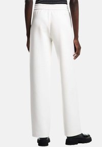 Pantaloni bianchi a gamba larga con vita elastica, realizzati in tessuto morbido. Presentano una superficie liscia e una linea dritta fino all'orlo.