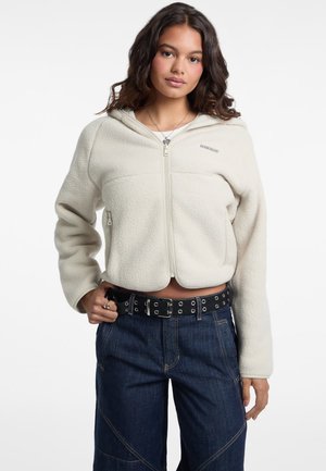 Felpa con cappuccio color crema in pile, con chiusura a zip davanti, polsini a coste e vestibilità rilassata. Presenta un logo sul petto e tasche laterali con zip.