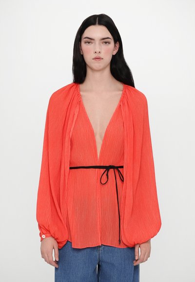 Blouse rouge plissée avec un décolleté en V profond, des manches longues et une ceinture noire à la taille. Le tissu semble léger et texturé.