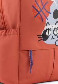 Sac à dos en tissu corail avec un graphisme de chat ludique ; comprend une fermeture éclair, une surface texturée et un détail de cordon de serrage bleu en accent.