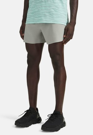 Grijze sportkorte broek met een lichtgewicht ontwerp, gecombineerd met zwarte sneakers met gestructureerde details en vetersluiting. Mintgroene top zichtbaar.