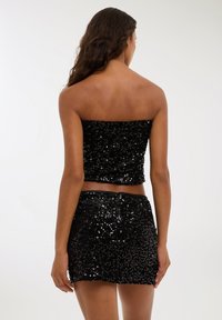 Set composto da top corto e mini gonna in paillettes nere con un design aderente. Tessuto liscio, top senza spalline e orlo corto sulla gonna.