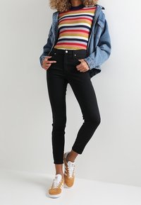 Suéter de rayas acanaladas en rojo, amarillo y azul marino, combinado con jeans negros de cintura alta y zapatillas de ante marrón con acentos blancos.