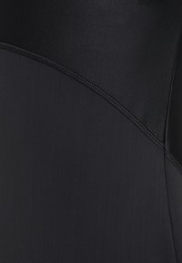 Schwarzer Stoff mit glatter Textur, der kontrastierende Bereiche und flache Nähte aufweist. Subtiler Glanz im Material, keine sichtbaren Muster oder Hardware.