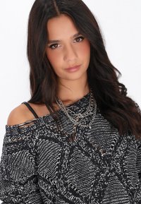 Pulover tricotat alb-negru cu umeri descoperiți, cu modele texturate. Un colier din lanț argintiu stratificat adaugă un detaliu metalic.