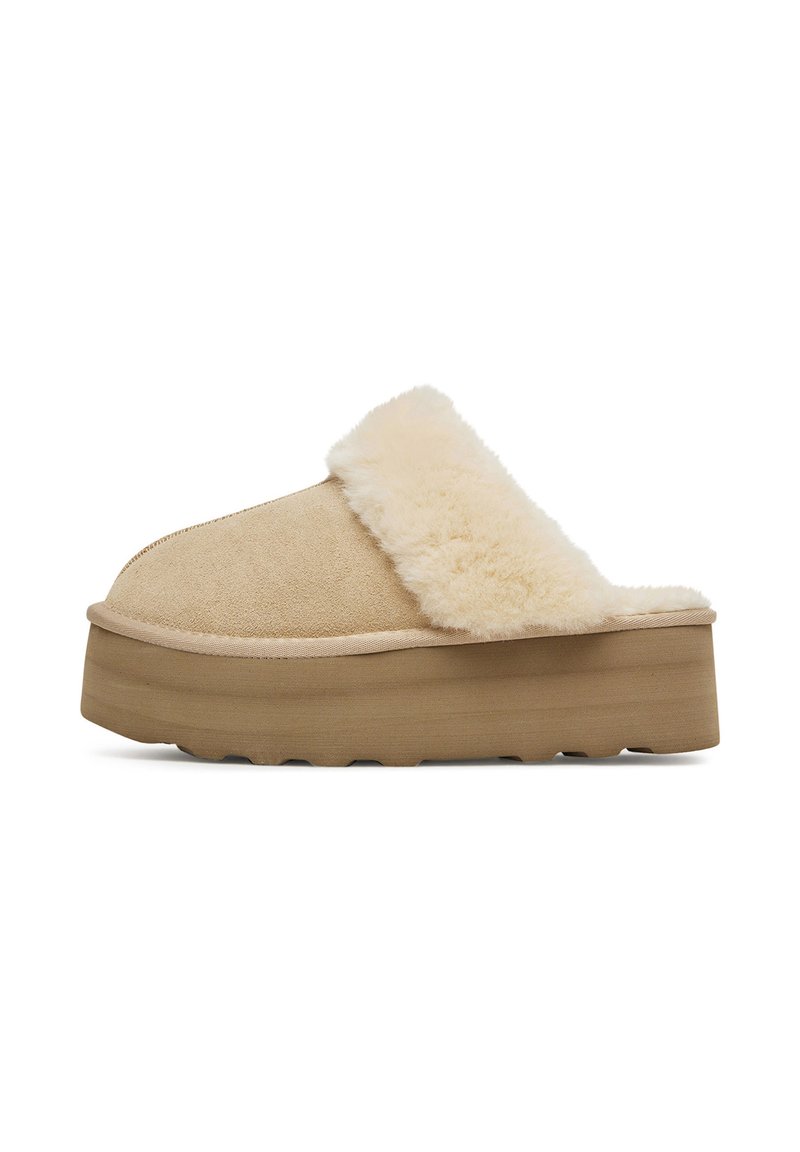 Bežové skluzné pantofle s plyšovou kožešinou a silnou platformou. Materiál je měkká semiš, strukturovaná a má minimalistický design.
