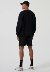 Felpa nera e pantaloni corti, vestibilità rilassata. Collo a giro, polsini a costine, abbinati a calzini neri e sneakers grigie. Stile atletico semplice.