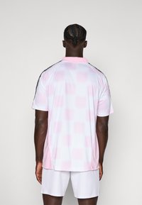 Polo shirt in het wit met een roze geblokt patroon, korte mouwen, roze kraag en zwarte zijstrepen, gemaakt van ademende stof.