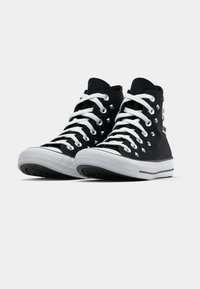 Adidași negri cu glezna înaltă, cu șireturi albe, talpă din cauciuc și cu cuie argintii pe laterale. Prezintă un material texturat și un vârf rotund clasic.