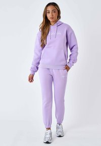 Lilak hoodie met een voorzak en koordjes, gecombineerd met bijpassende joggers. Kenmerkt zich door elastische cuffs en subtiele witte logo-accenten.