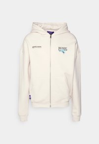 Krémová zipová mikina vyrobená z měkké tkaniny. Obsahuje kapuci se stahovací šňůrkou, přední kapsy a potištěný text a grafiku na hrudi.