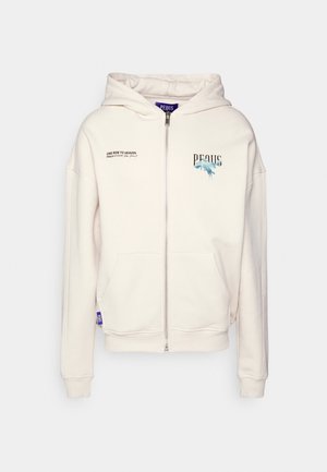 Crème-kleurige zip-up hoodie gemaakt van zachte stof. Heeft een capuchon met trekkoord, voorzakken en bedrukt tekst en grafische afbeeldingen op de borst.
