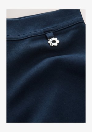 Mornarsko modra tkanina z gladko teksturo, okrašena s srebrnim gumbom v obliki cvetlice blizu pasu. Preprost in čist dizajn.