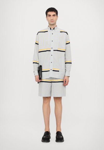 Chemise rayée et short en bleu clair, jaune et noir. La chemise présente un design à boutons, des manches longues et une poche poitrine. Chaussures noires.