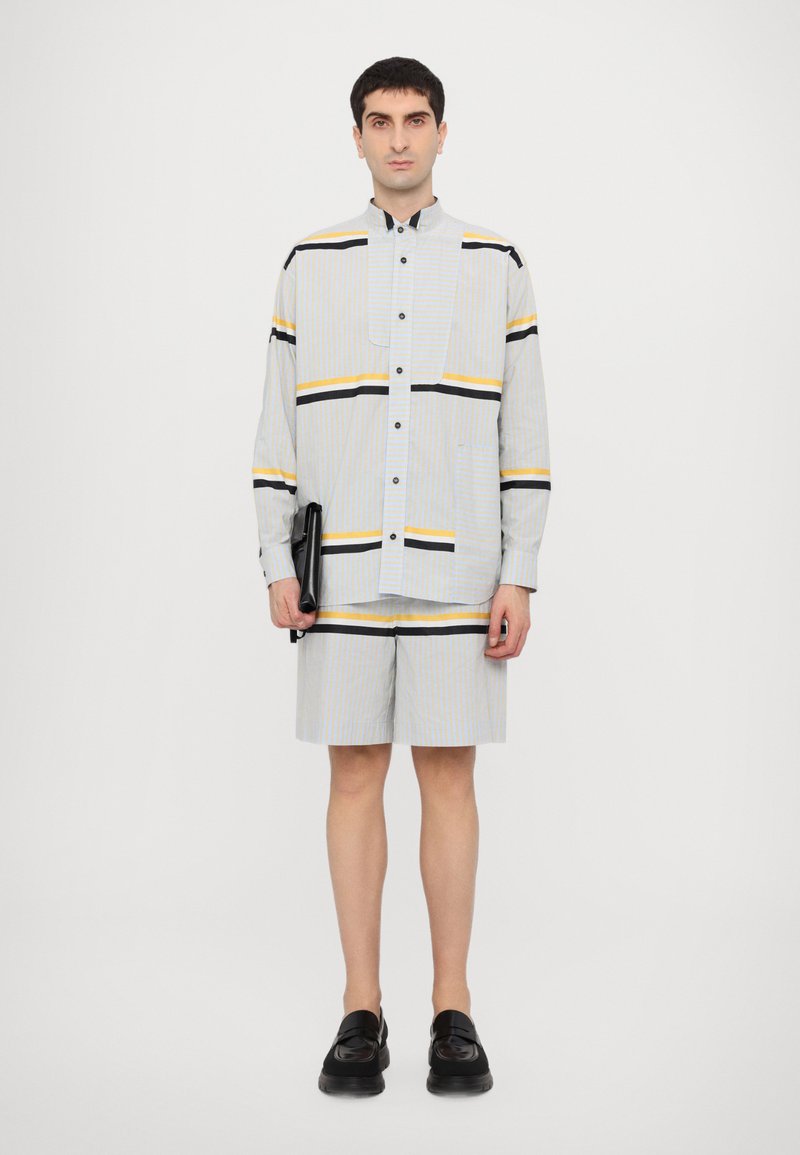 Rutet skjorte og shorts i lys blå, gul og svart. Skjorten har en knapp-op design, lange ermer og en brystlomme. Svarte sko.