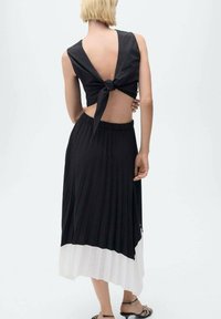 Černý crop top s vazbou na zádech, spárovaný s plisovanou maxi sukní v černobílé kombinaci. Design obsahuje odhalená záda a elastický pás.
