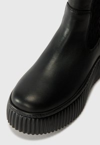 Bottine en cuir noir à bout arrondi, avec une semelle texturée et une plateforme en caoutchouc noir striée. Fini lisse et détails de design minimalistes.
