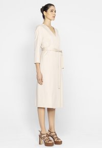 Beżowa sukienka kopertowa z rękawami o długości 3/4, z zaznaczoną talią i prostym krojem. W połączeniu z brązowymi sandałami na platformie.