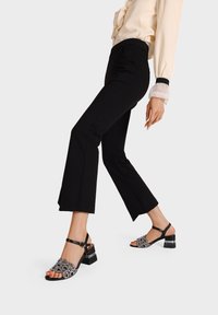 Sandali neri con tacco, decorati con un design floreale, punta aperta e cinturino alla caviglia. Parte superiore tessurizzata con riflessi lucidi; tacco a blocco.