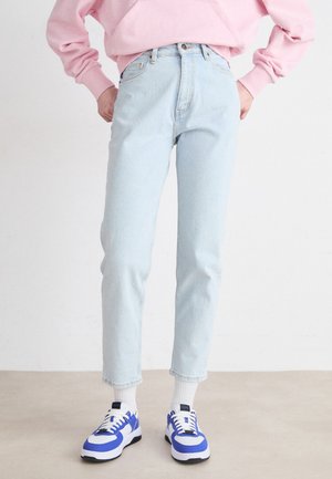 Lyseblå, høyt midjeførte jeans med avsmalnet passform, kombinert med hvite og blå sneakers. Jeansene har en falmet, myk denimtekstur.