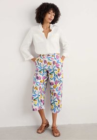 White linen shirt with v-neck and two front pockets; cropped pants featuring a colorful floral pattern in purple, yellow, and blue. Brown sandals.