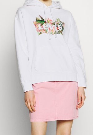 Witte hoodie met een bloemenprint Levi's-logo, gecombineerd met een roze denim rok, gedragen door een persoon met ontspannen handen langs het lichaam.
