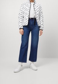 Vit pufferjacka med svart handskriven text, ihop med högmidjade blå denimvidben byxor och vita sneakers.