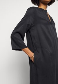 Musta, polvipituinen mekko, jossa on pyöreä pääntie ja 3/4-hihat. Contains sivutaskut ja se on tehty sileästä, kevyestä kankaasta. Yksinkertainen muotoilu.