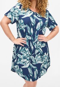 Marinblå blommig klänning med korta ärmar, rund halsringning och avslappnad passform. Tyget har en mjuk textur med stora gröna och vita blommönster.