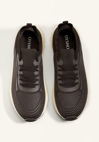 Zwarte sportschoenen met een gestructureerde bovenkant, voorzien van gestreepte accenten, tonale veters en een lichte zool.
