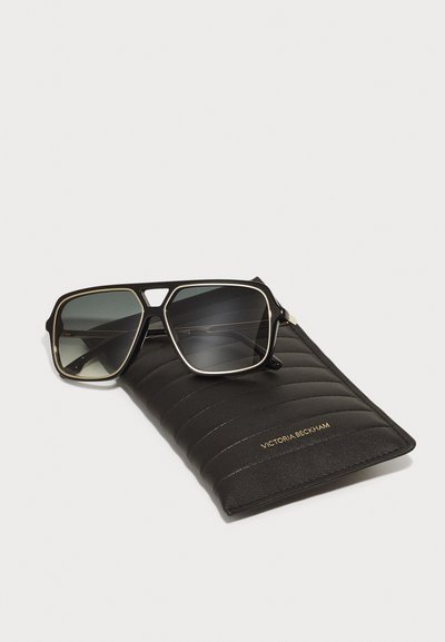 Svarta solglasögon med grå linser, fyrkantiga bågar och guld accenter, vilande på ett svart quiltat fodral med guld branding.