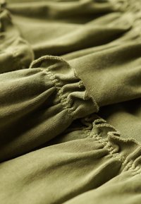 Olijfgroen stof met gathered ruffles, die een textuur oppervlak en zichtbare stiksels laat zien. Zacht, vallend materiaal in close-up weergave.